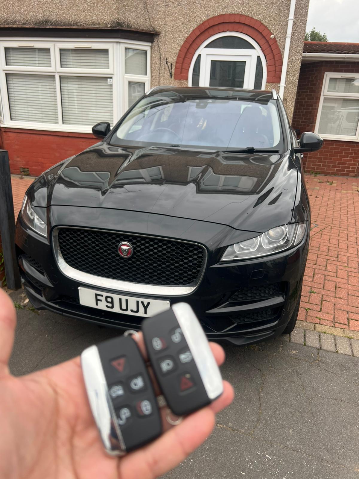 Two replacement Jaguar F-Pace smart keys held in front of the vehicle on a residential driveway